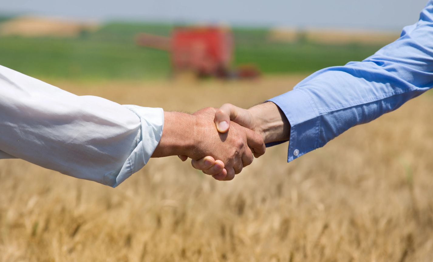 Поддержка сельскохозяйственной кооперации. Рукопожатие на фоне поля. Рукопожатие фермеров. Пожатые руки на фоне поля. Рукопожатие сельское хозяйство.